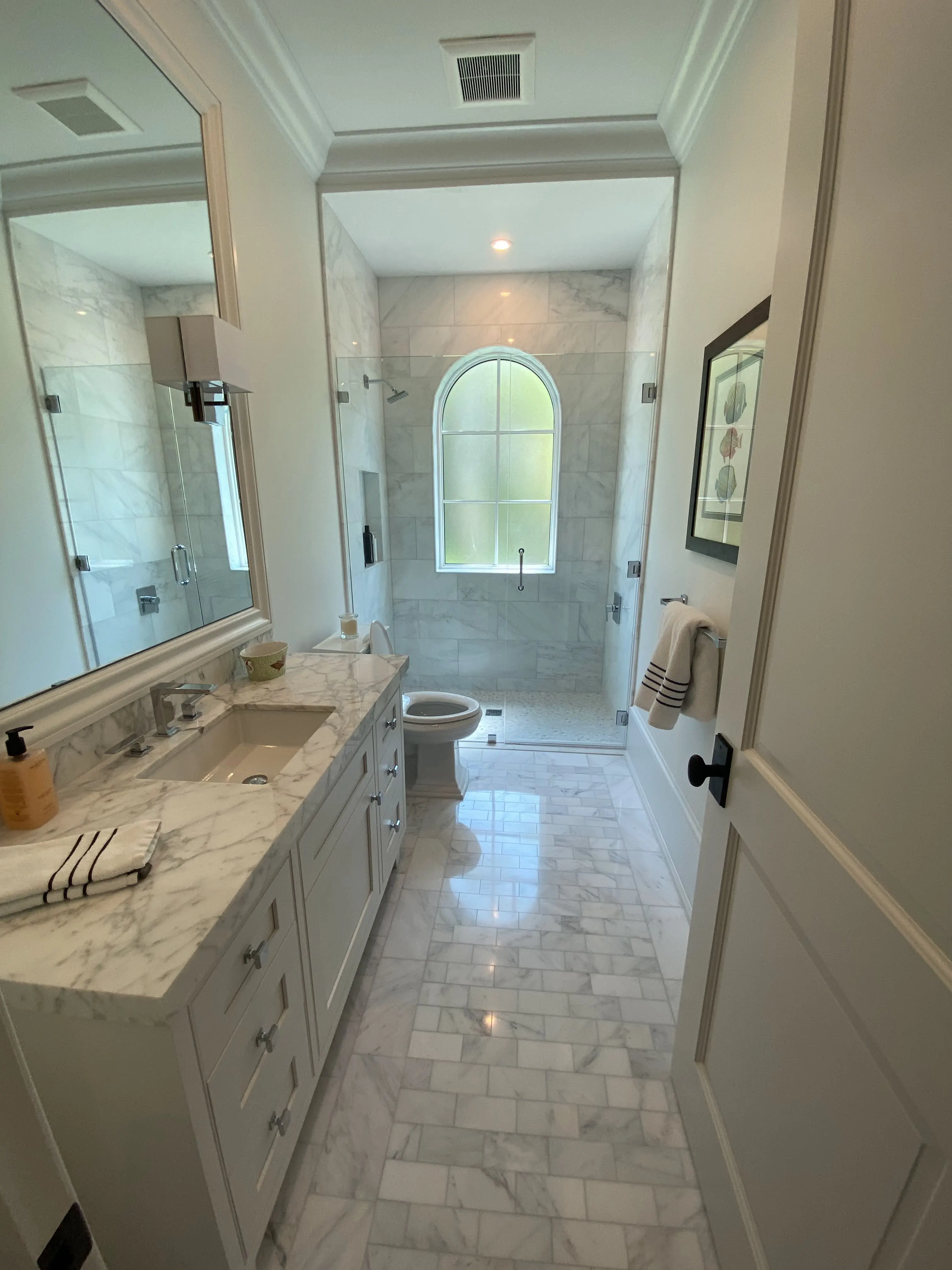 This bathroom features luxurious Carrera marble throughout, with classic subway marble tiles on the walls, a marble-tiled shower, and a coordinating marble vanity and flooring, creating a cohesive and timeless design.