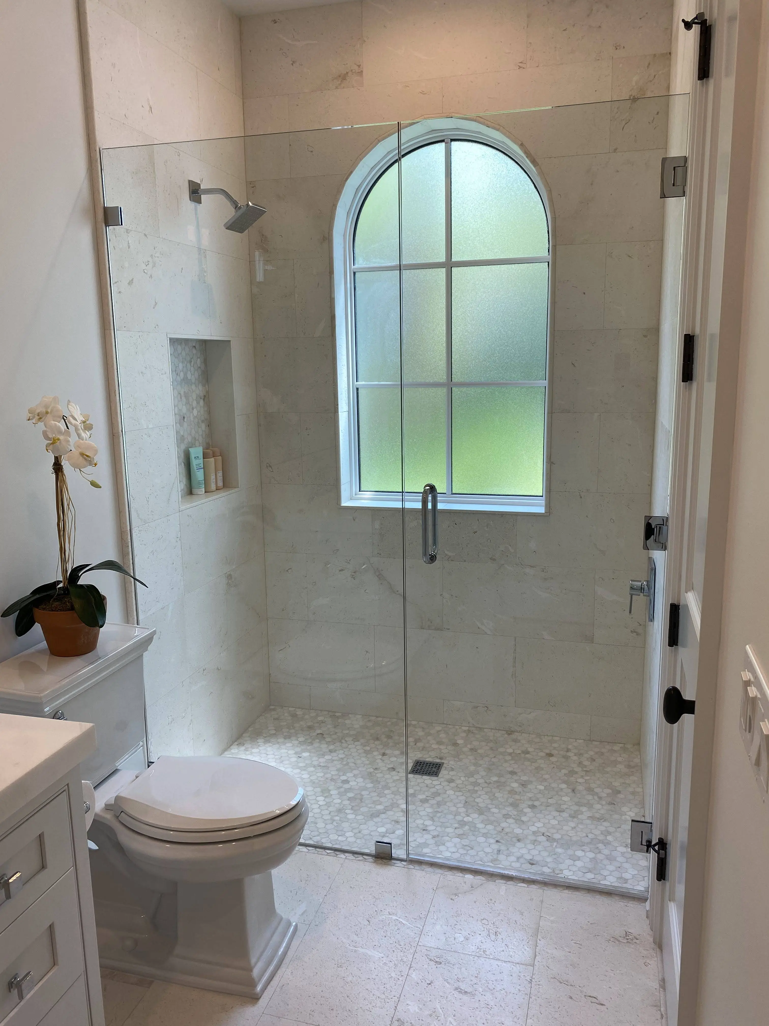 Beautiful marble shower with a mosaic tile floor, expertly installed with precision around the unique arched window, creating a sleek and timeless design for a serene bathing experience.