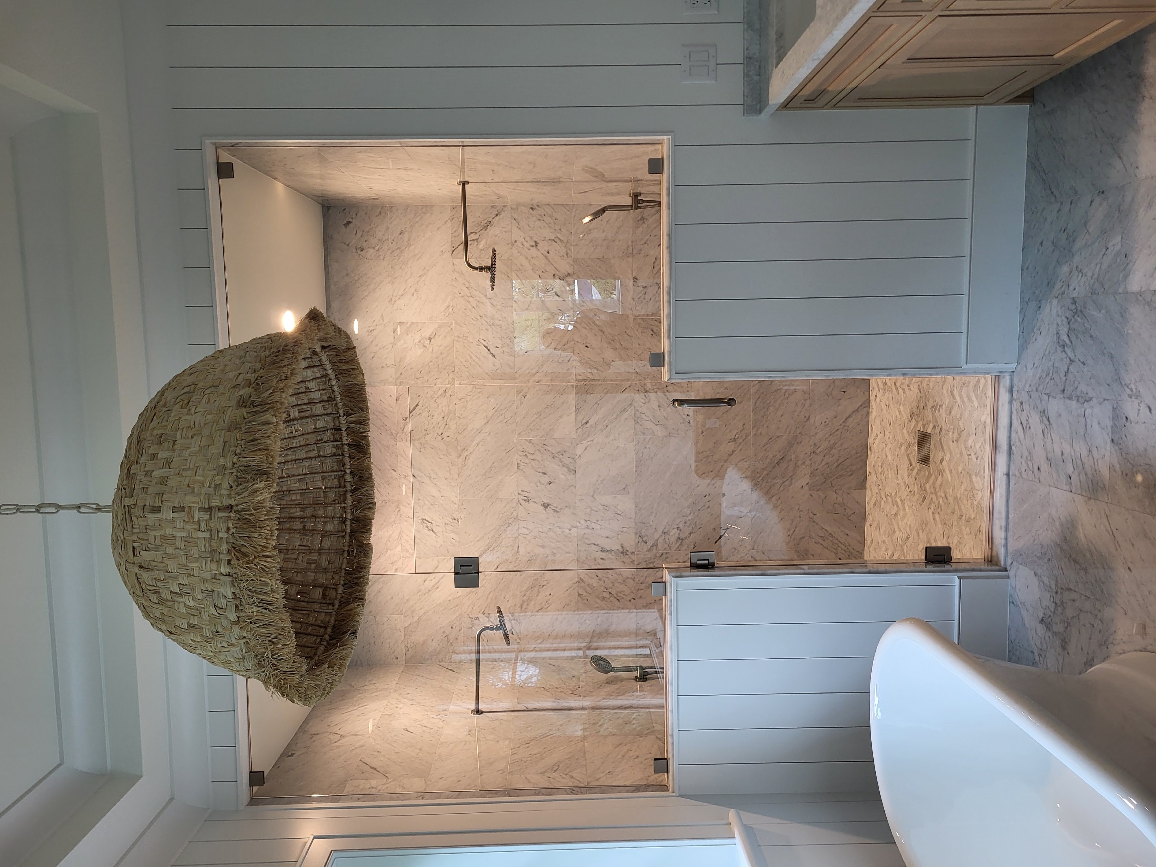 This luxurious beach mansion bathroom features a White Carrera marble shower with a staggered joint pattern, enclosed by elegant glass and knee walls, perfectly complementing the serene and coastal design.