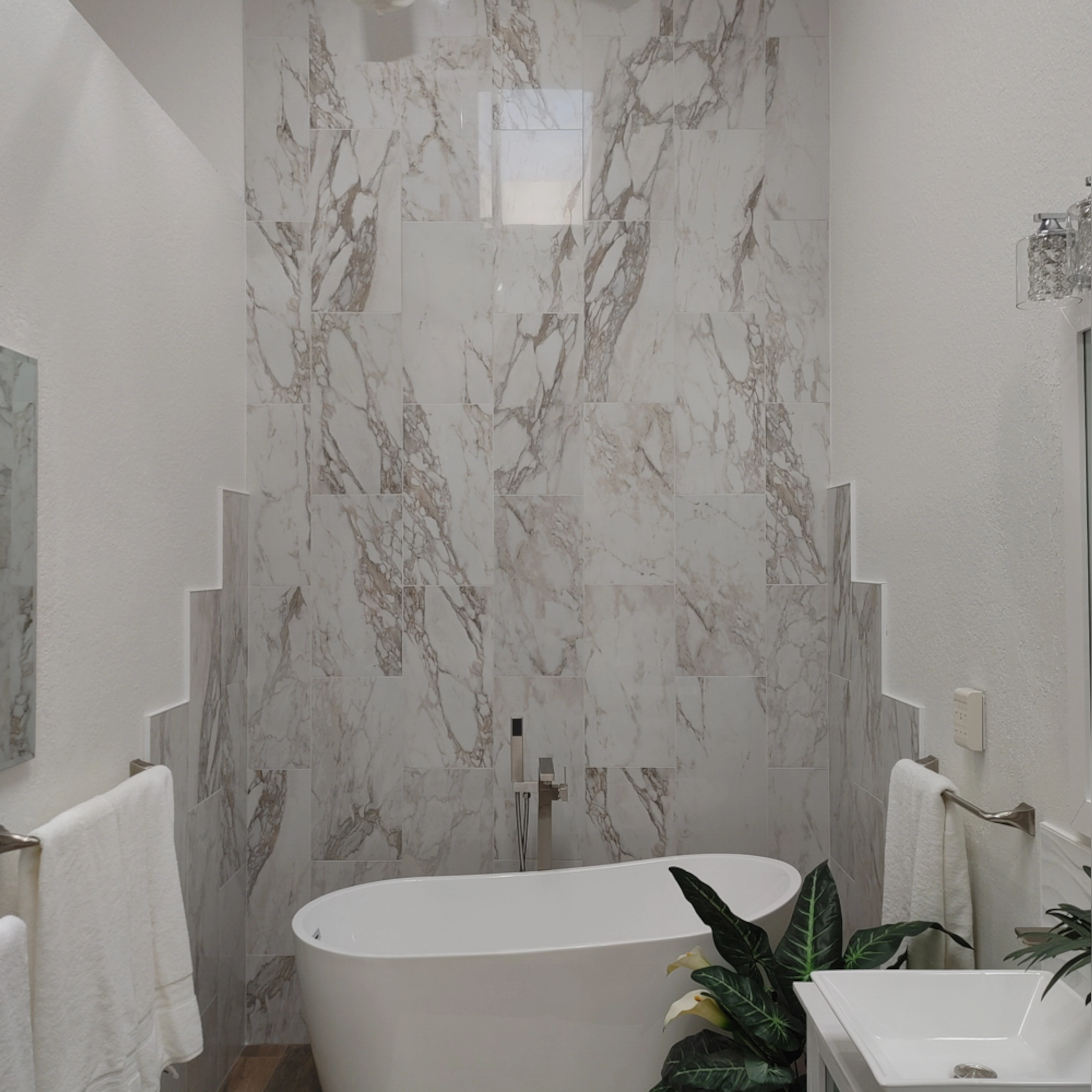 This elegant bathroom features porcelain tiles with a bold marble-like pattern, creating a striking accent wall that frames the freestanding tub beautifully with a unique stair-stepped border.