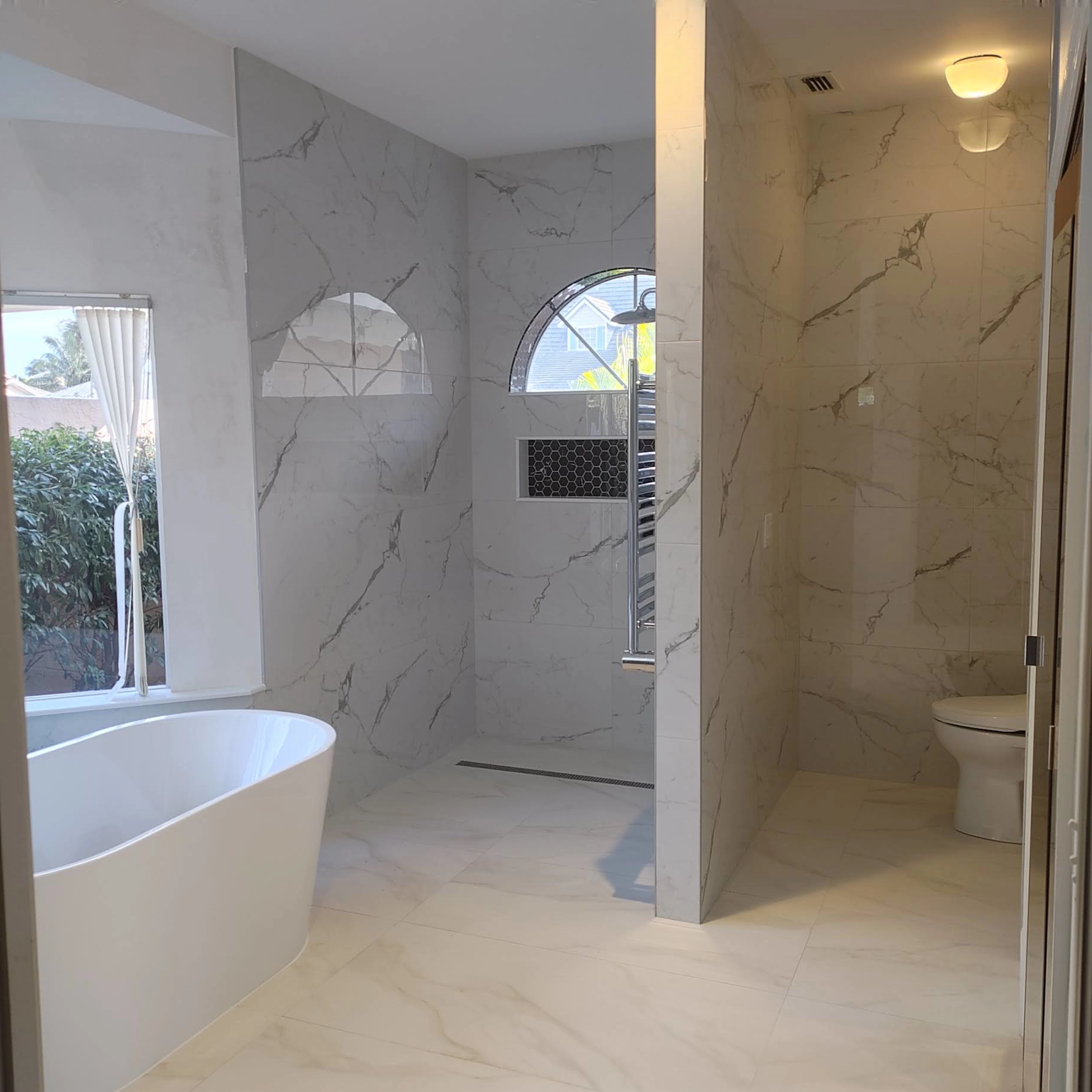 This bathroom features sleek porcelain tiles throughout, with a Zero Entry shower designed for seamless accessibility, highlighted by a linear drain and a contrasting tile niche for added functionality and style.