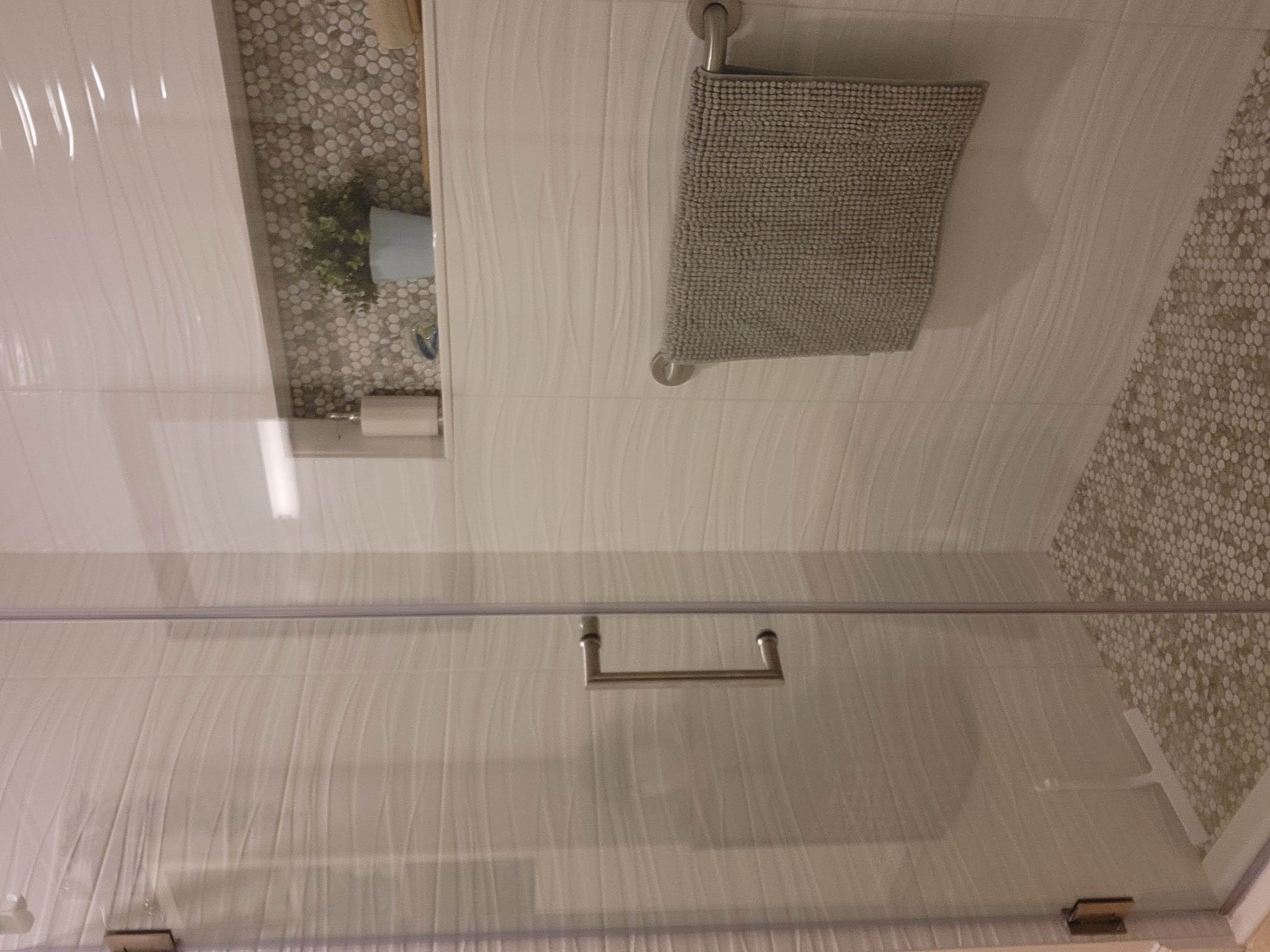 This shower features sleek textured tiles with a wavy design on the walls, complemented by a mosaic penny tile floor in neutral tones. A recessed niche with matching mosaic accents adds functionality and a cohesive, modern aesthetic to the space.