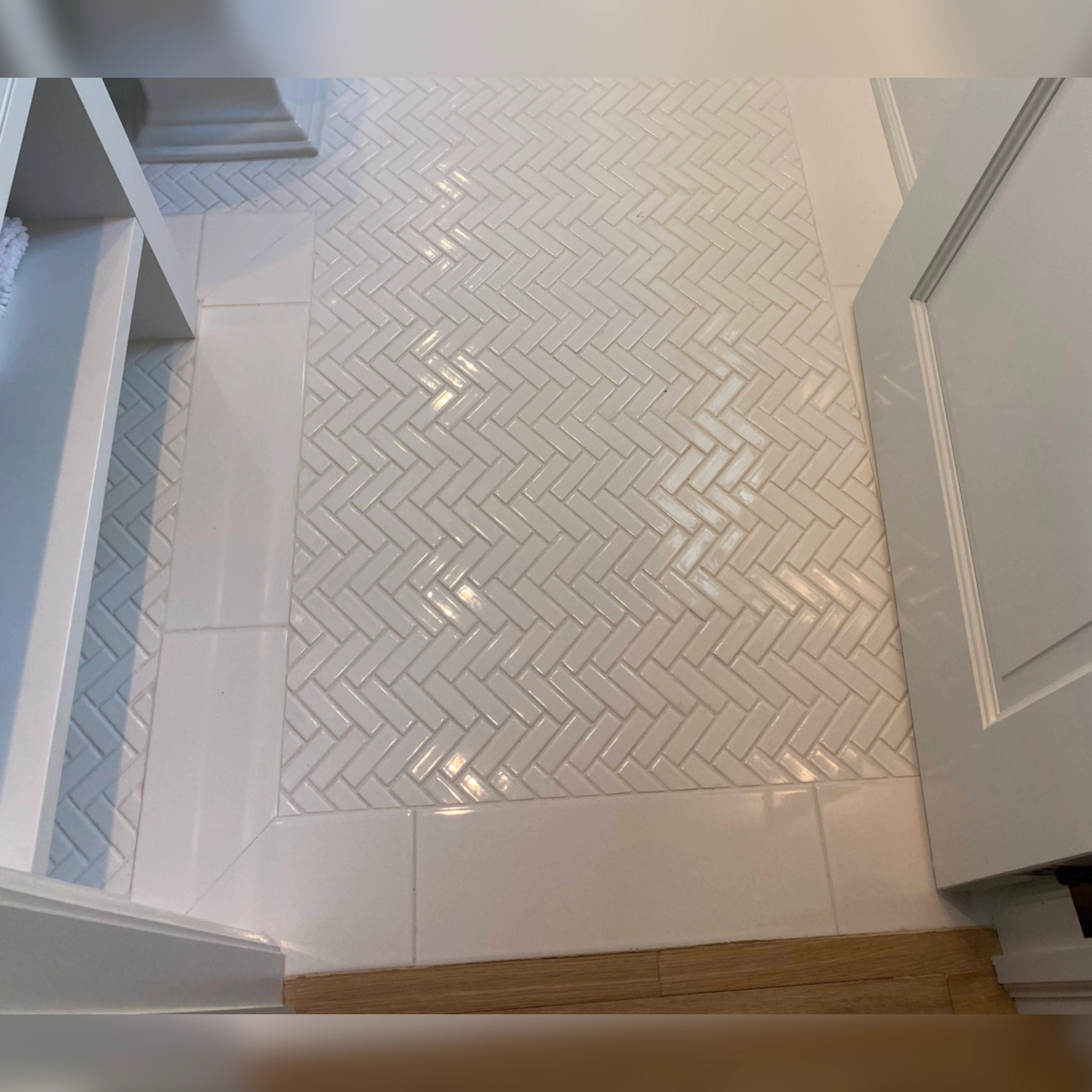 This floor features elegant porcelain herringbone mosaic tiles installed diagonally, framed with a clean, rectangular tile border for a polished and defined finish, adding both texture and sophistication to the space.