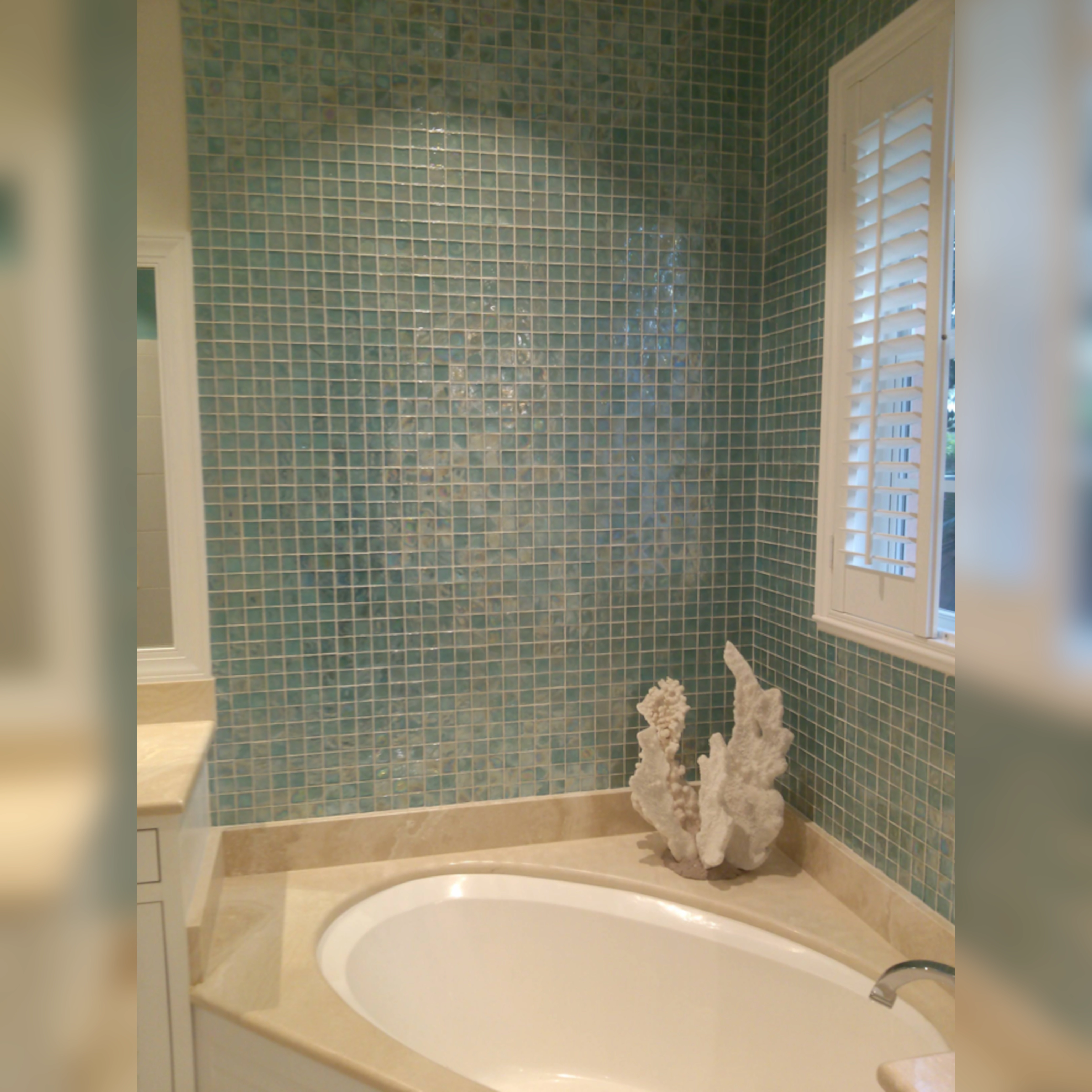 This serene tub surround is adorned with shimmering glass mosaic tiles in soft aqua tones, creating a calming, spa-like atmosphere that reflects light beautifully and adds a touch of elegance.