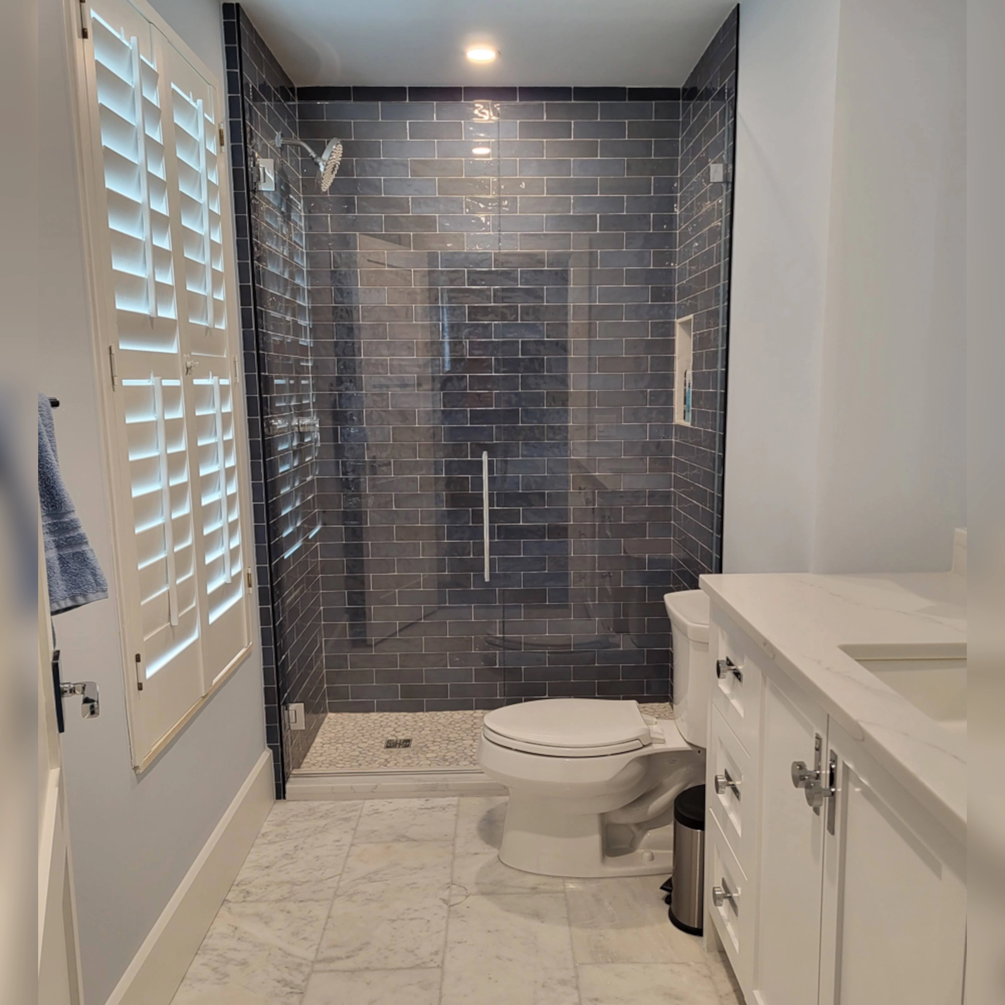 The shower features sleek, glossy dark subway tiles arranged in a classic offset pattern, accented by clean grout lines for a polished look, while a glass enclosure and built-in niche add modern functionality and style.