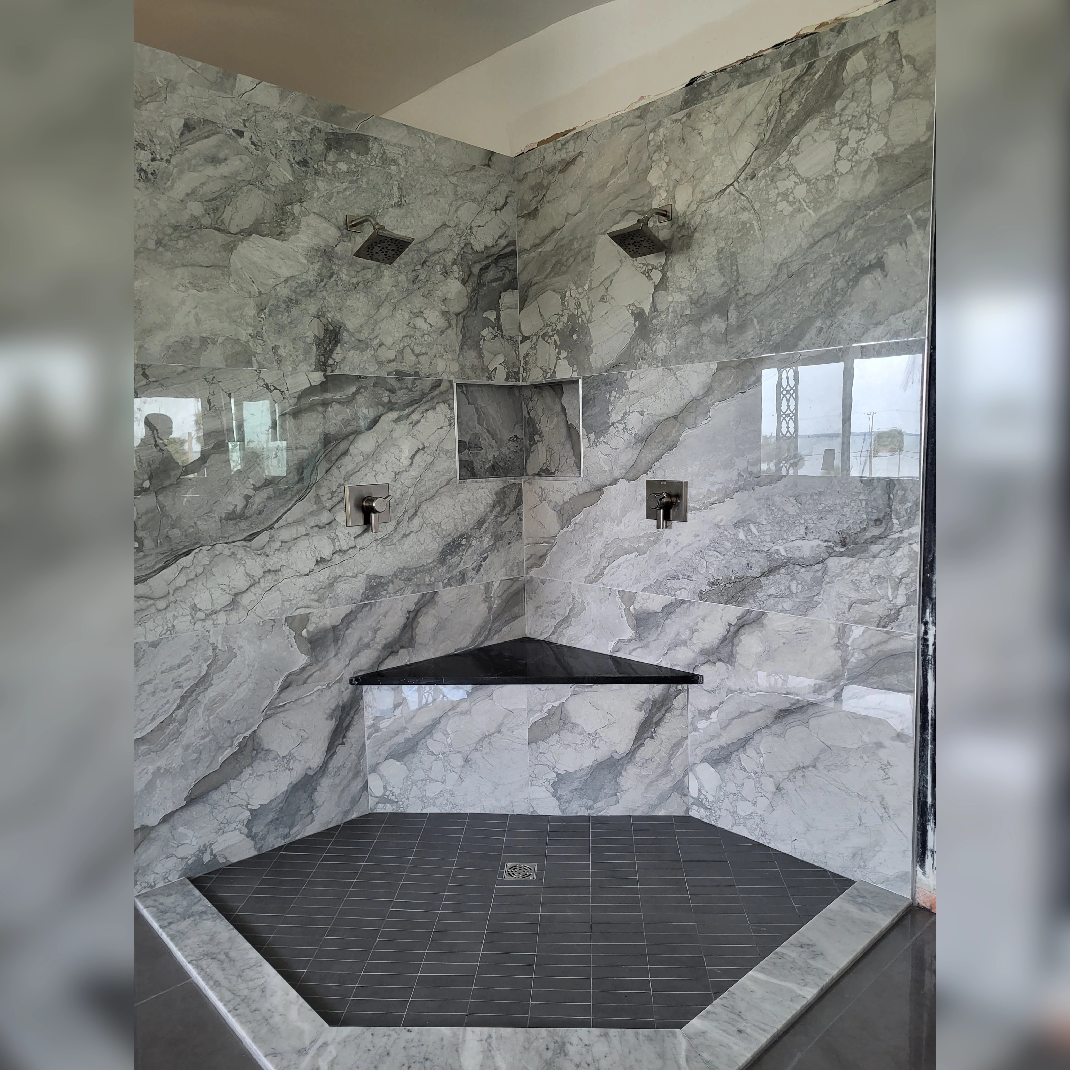 This shower features striking large-format porcelain tiles with dramatic veining, creating a seamless and luxurious look, complemented by a black accent bench and niche for both style and functionality.