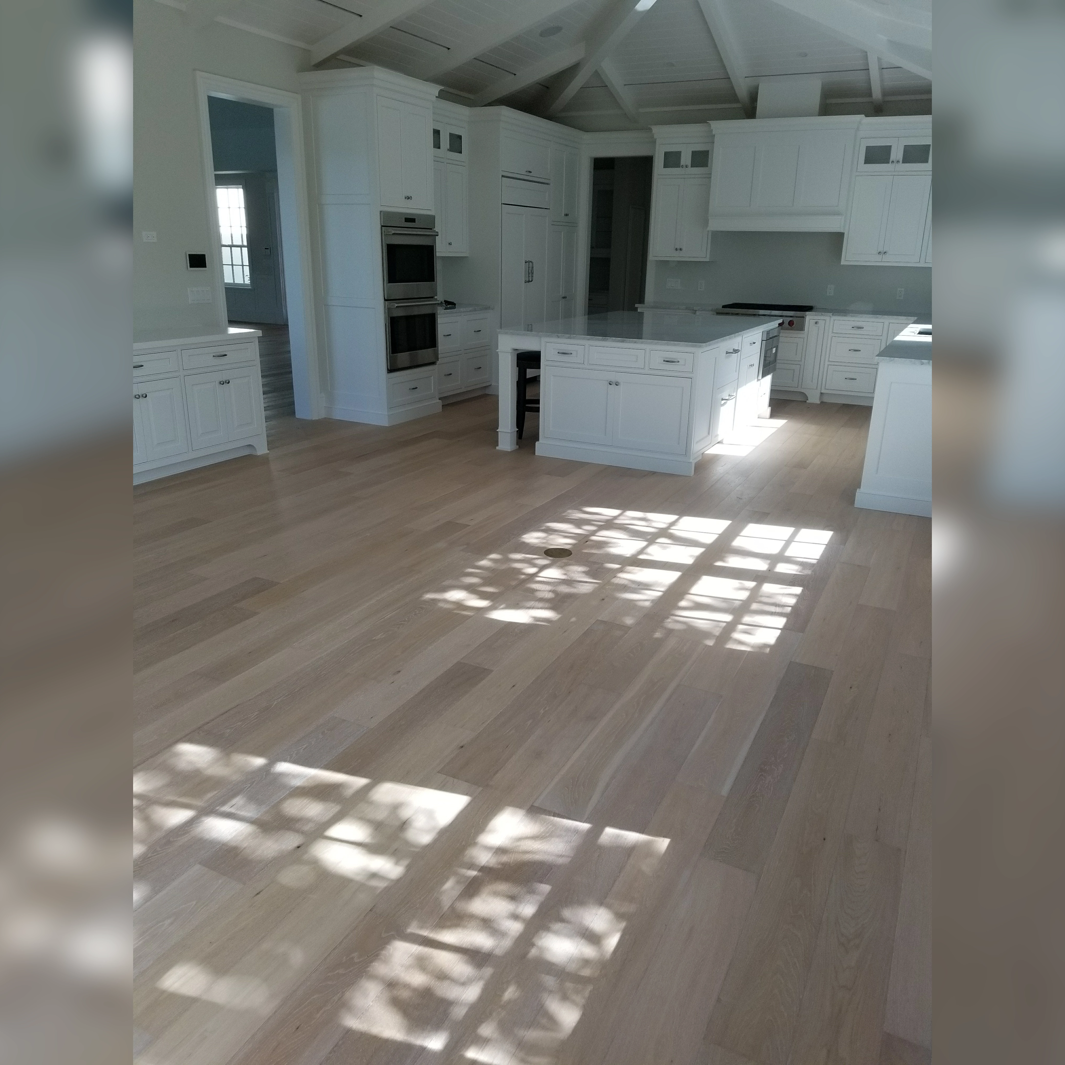 This bright kitchen features wide-plank engineered wood flooring with a light, natural finish that enhances the airy atmosphere, beautifully complementing the vaulted ceiling and crisp white cabinetry.