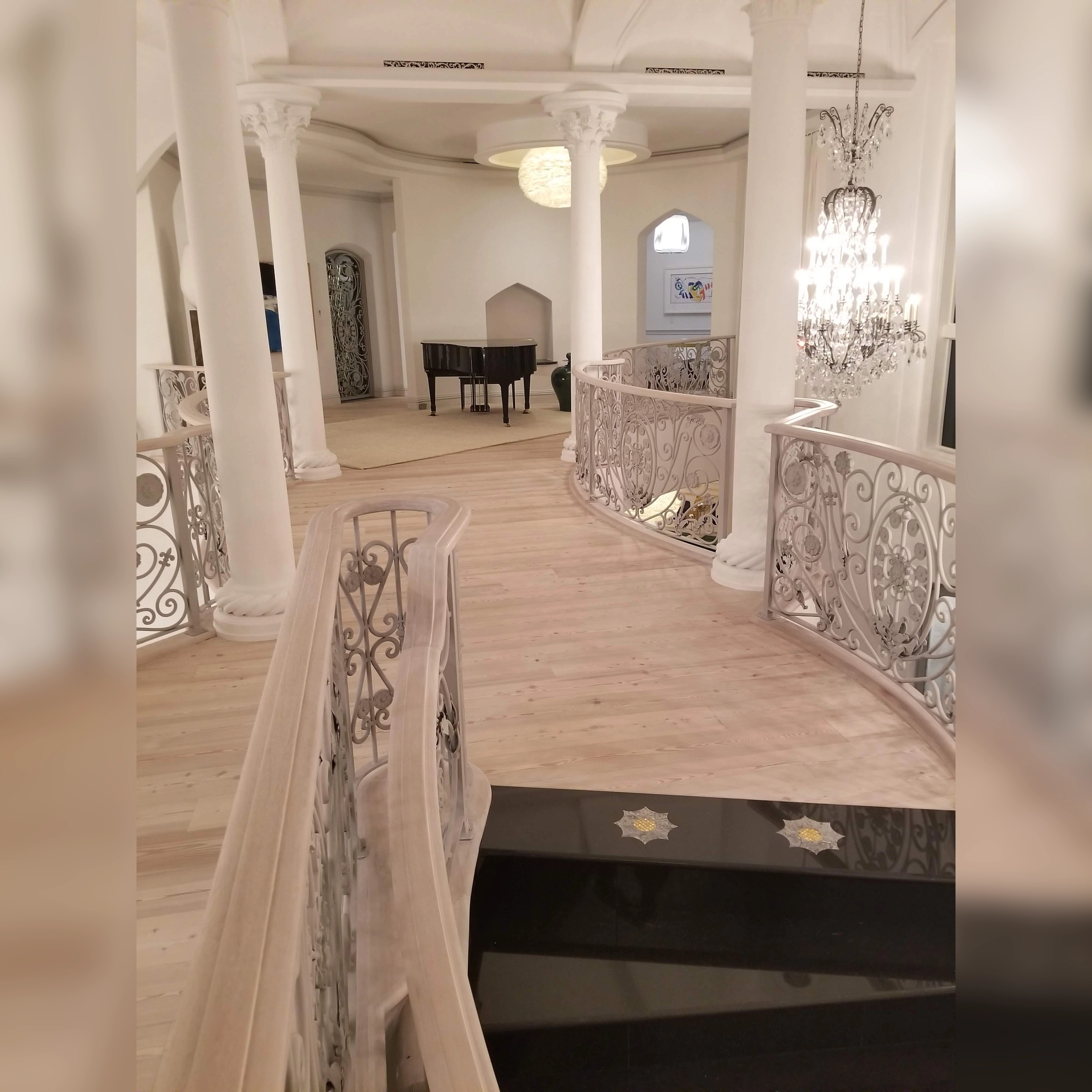 This stunning wood flooring showcases light, natural planks with a smooth finish, featuring intricate cuts that seamlessly follow the curved railings and grand architectural details, highlighting the craftsmanship and precision of the installation.