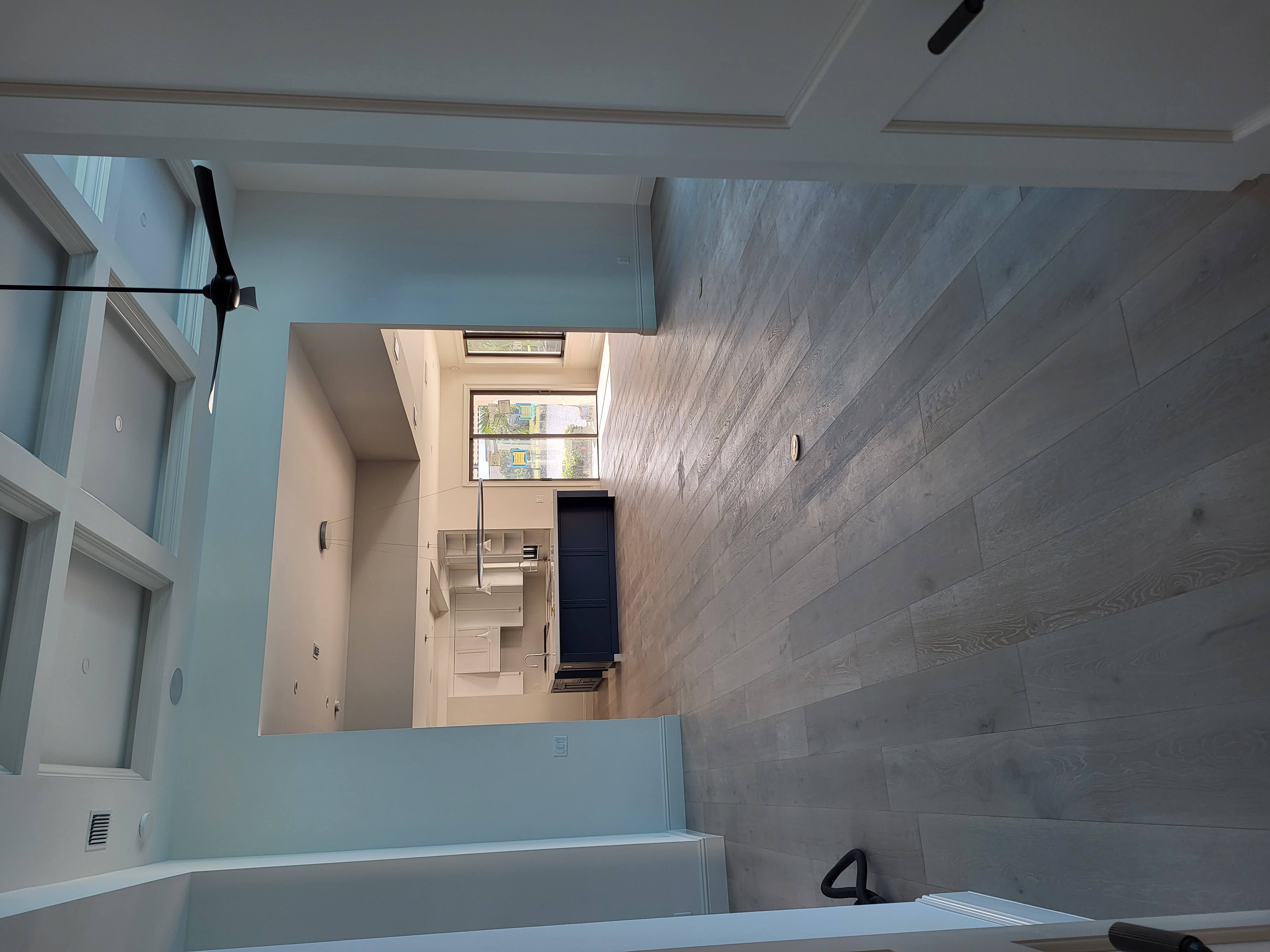 This space features engineered wood flooring in wide planks with a soft, gray-toned finish, creating a modern and cohesive flow between the living and kitchen areas, while complementing the coffered ceiling and clean architectural lines.