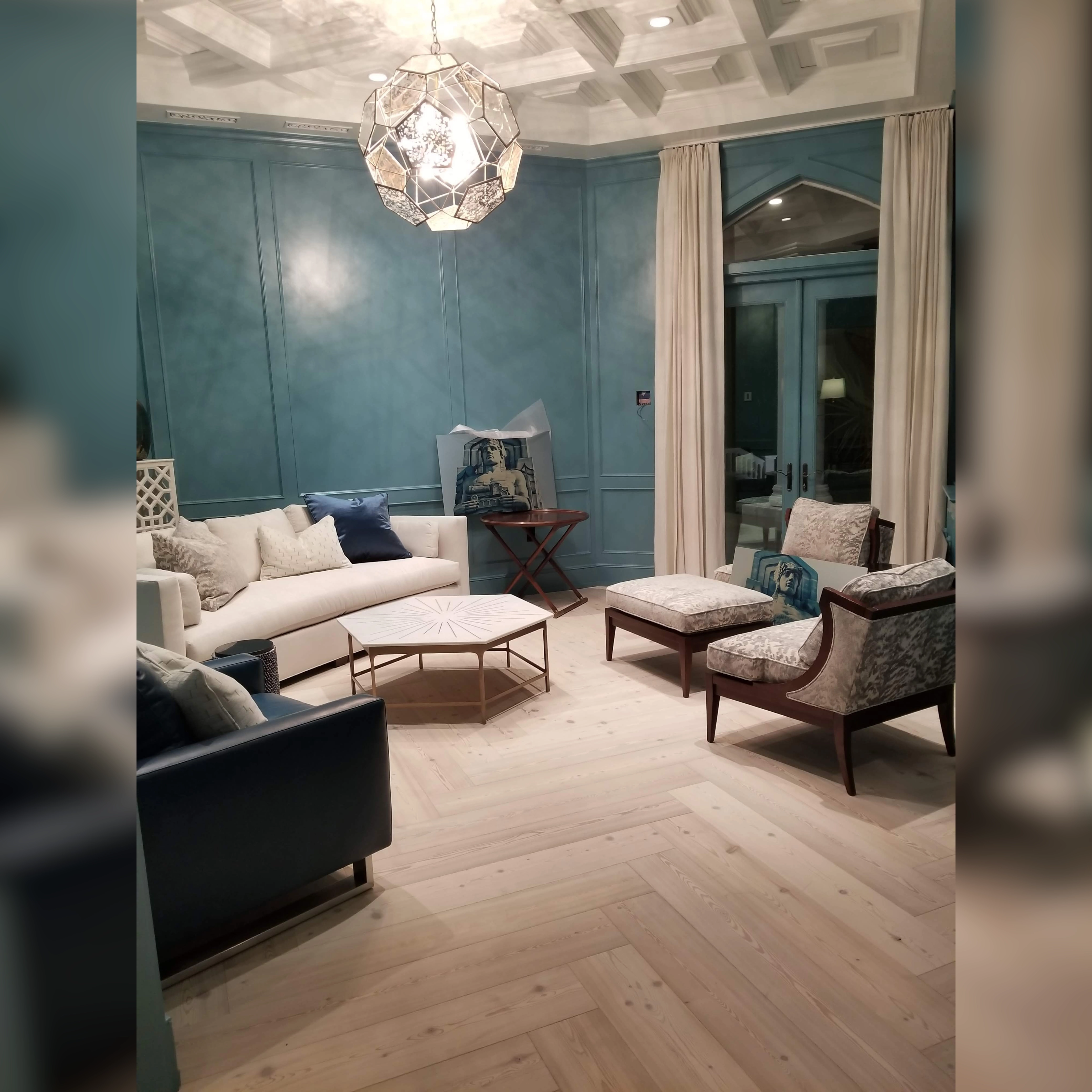 This elegant sitting room showcases a striking herringbone-patterned light wood floor(Engineered Wood), complemented by rich teal paneled walls, a coffered ceiling, and a modern geometric chandelier, creating a refined yet cozy ambiance.