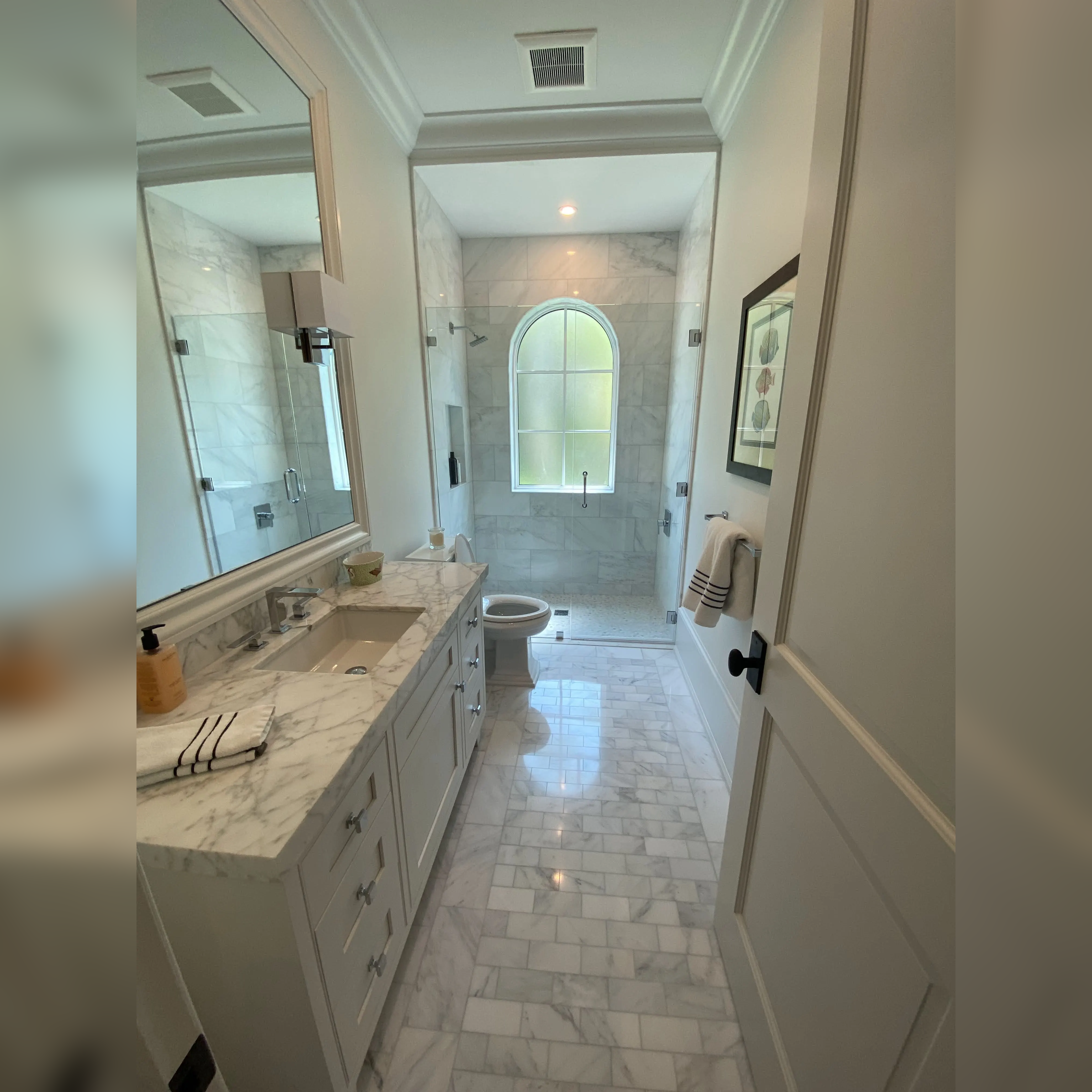 This bathroom features luxurious Carrera marble throughout, with classic subway marble tiles on the walls, a marble-tiled shower, and a coordinating marble vanity and flooring, creating a cohesive and timeless design.