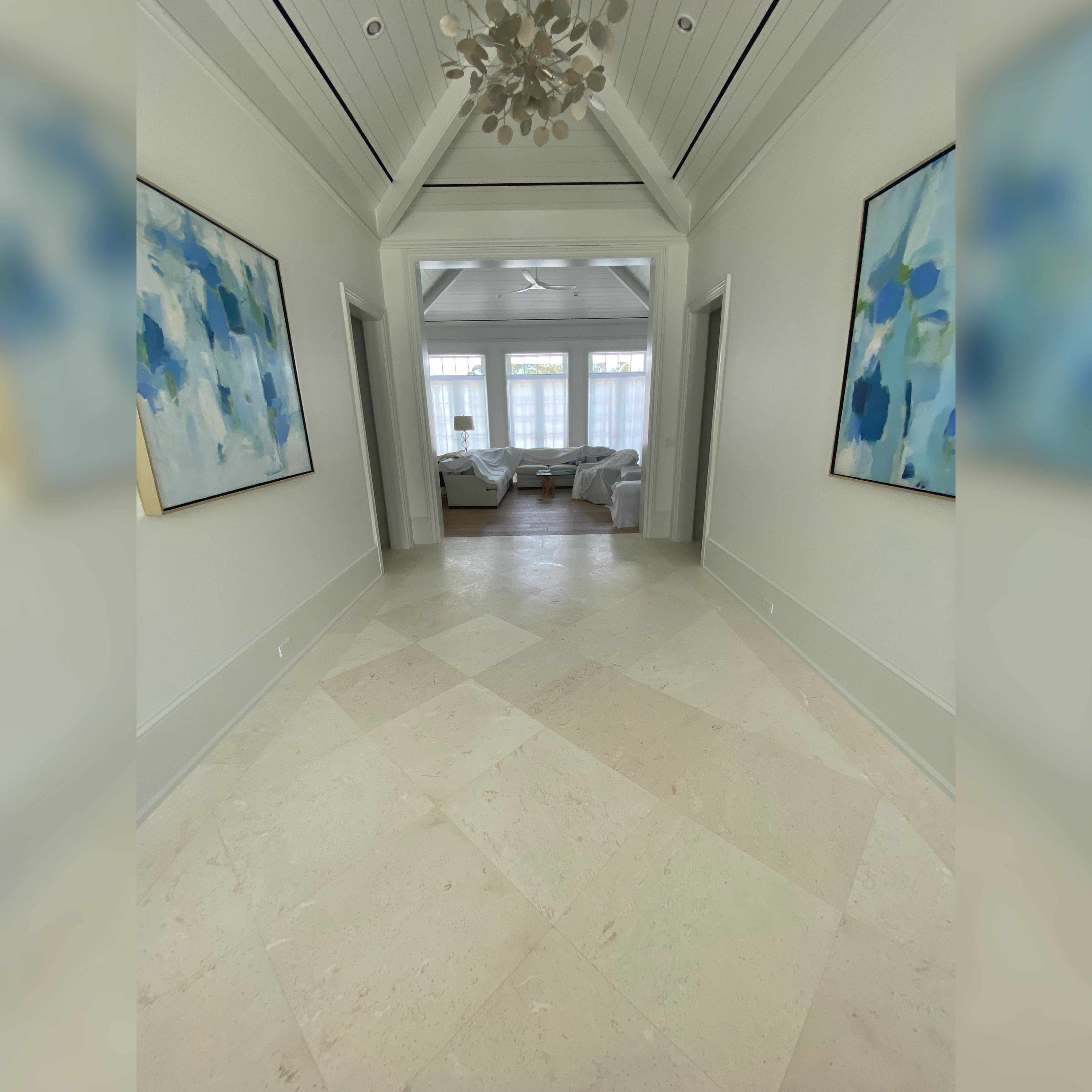 This foyer features elegant limestone marble flooring, laid in a diamond pattern that enhances the bright and spacious feel of the space, perfectly complementing the high-vaulted ceiling and contemporary decor.