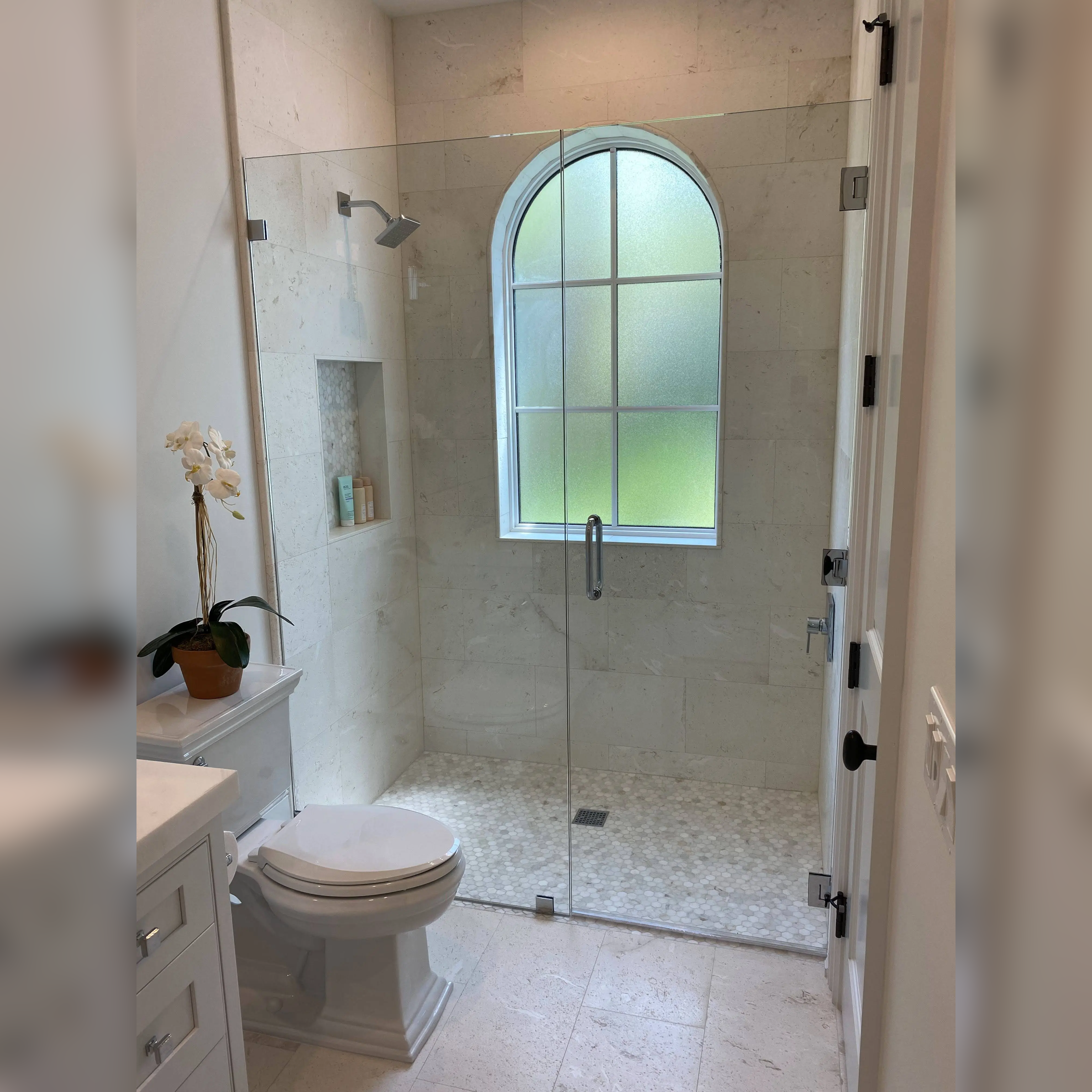 Beautiful marble shower with a mosaic tile floor, expertly installed with precision around the unique arched window, creating a sleek and timeless design for a serene bathing experience.