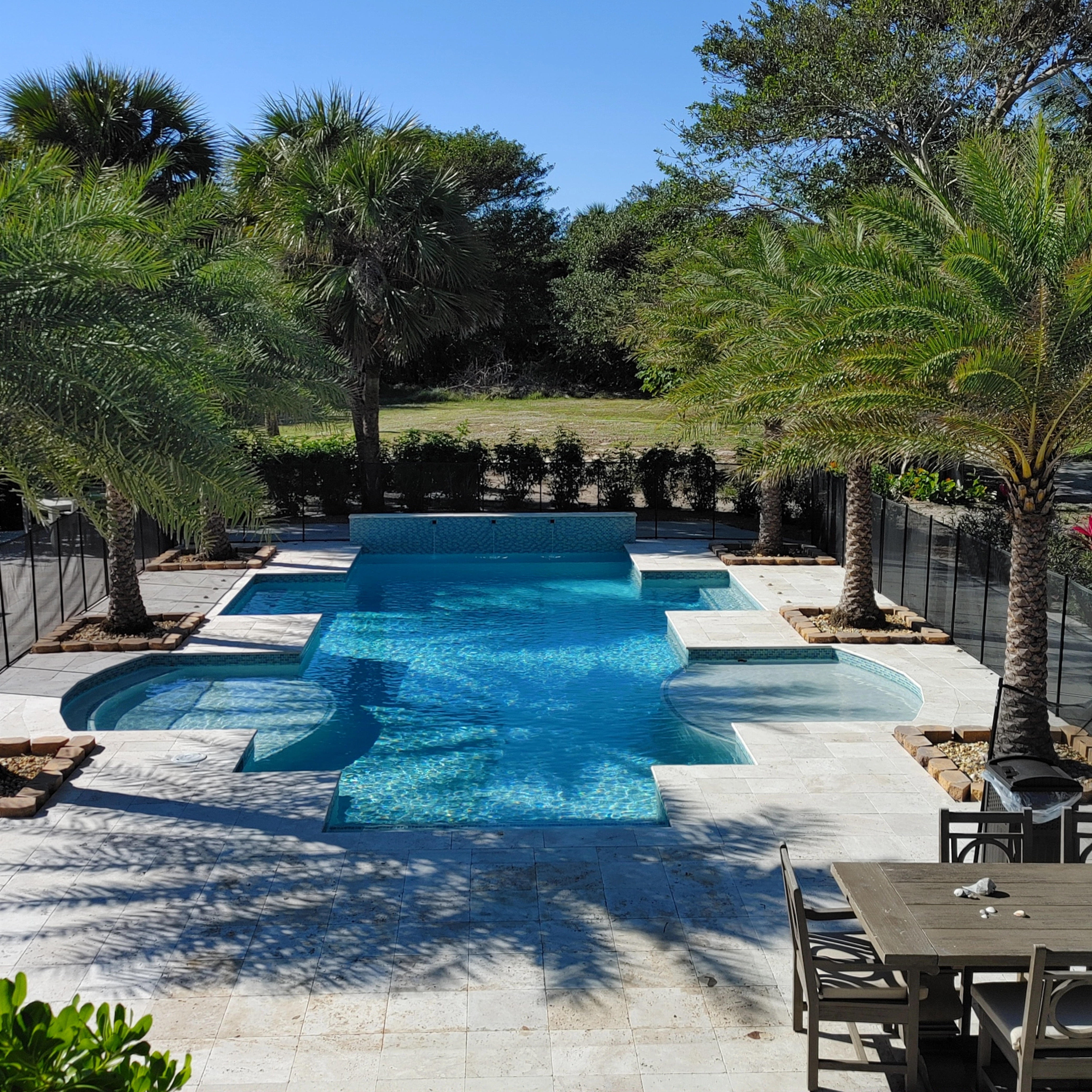 This stunning outdoor space features travertine pavers for the pool deck with a timeless, natural finish, expertly installed with radius coping that seamlessly follows the pool's curves.