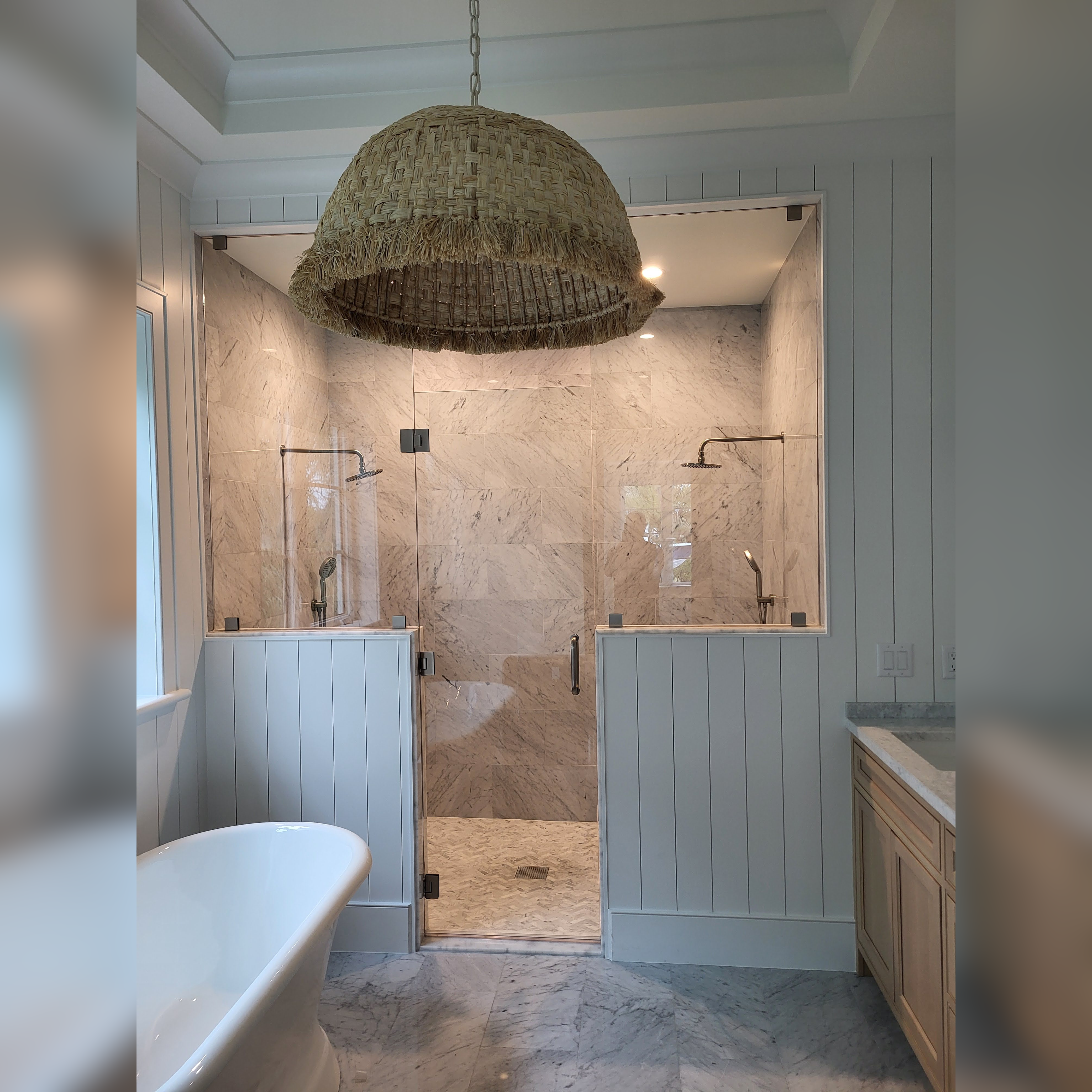 This luxurious beach mansion bathroom features a White Carrera marble shower with a staggered joint pattern, enclosed by elegant glass and knee walls, perfectly complementing the serene and coastal design.