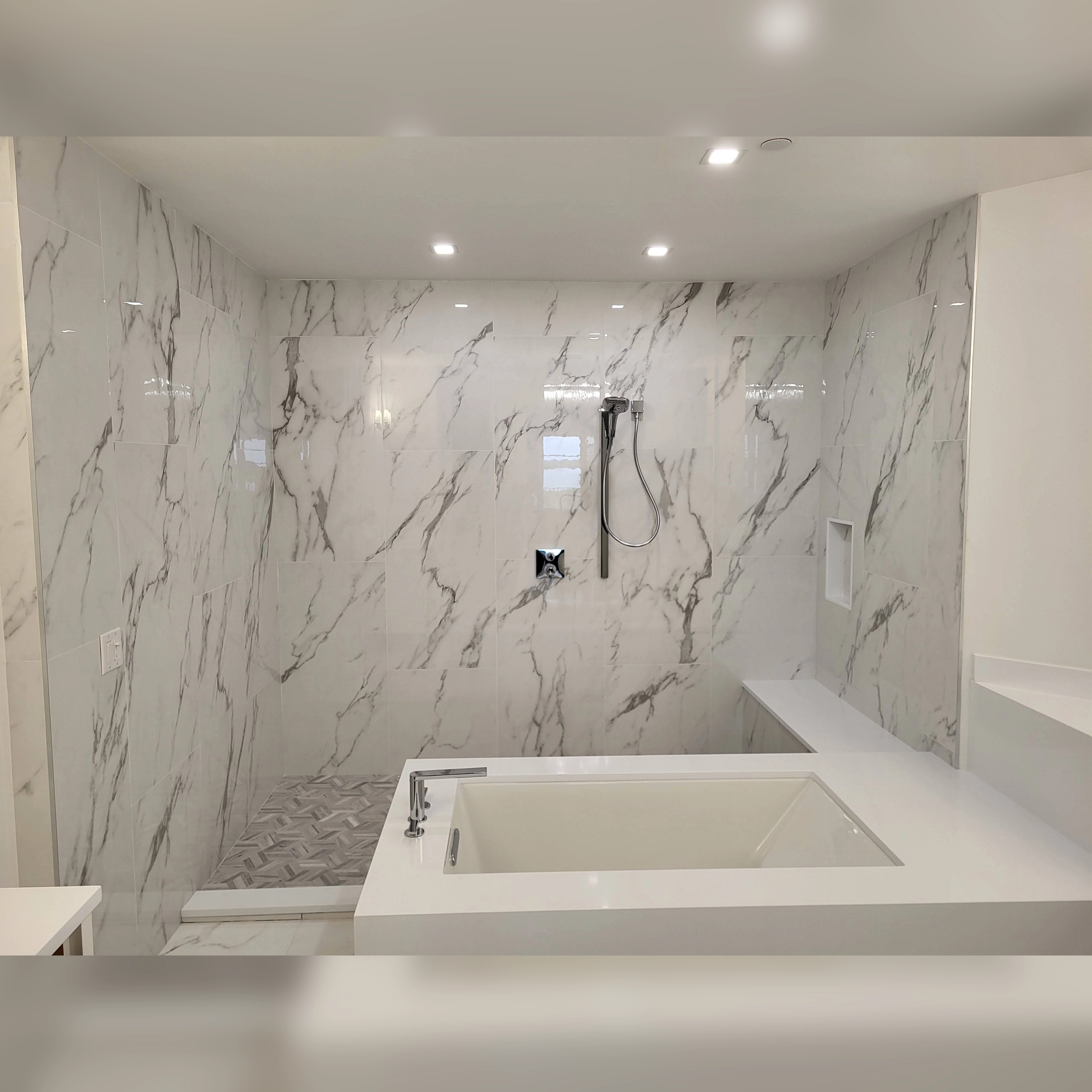 This bathroom features large 2 ft by 4 ft porcelain tiles with a marble-like pattern, seamlessly installed in the shower and surrounding the tub, creating a clean and modern aesthetic with minimal grout lines.