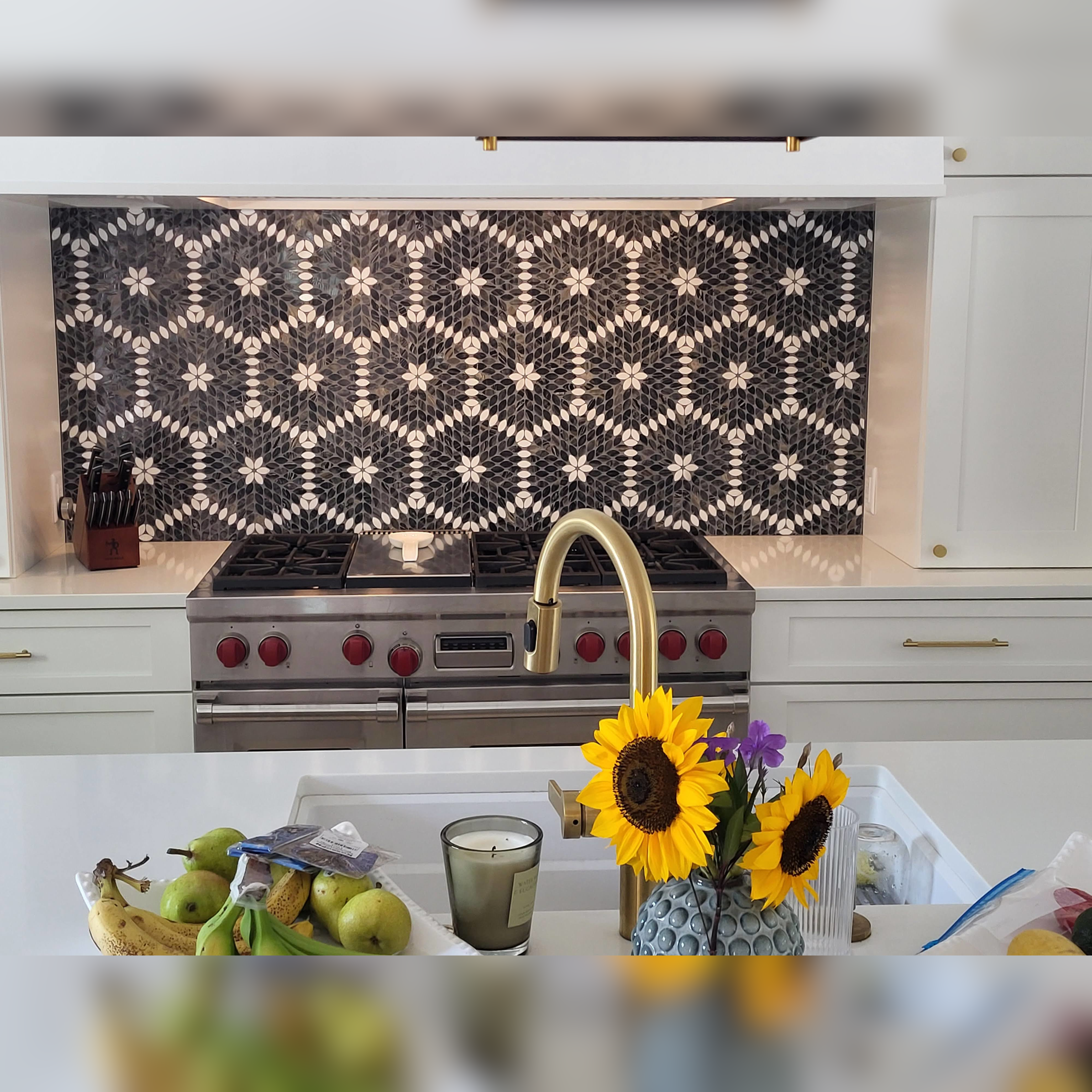 This kitchen backsplash features a striking mosaic tile design with intricate geometric patterns in contrasting black, white, and gray tones, serving as a bold focal point that beautifully complements the stainless steel appliances and crisp white cabinetry.