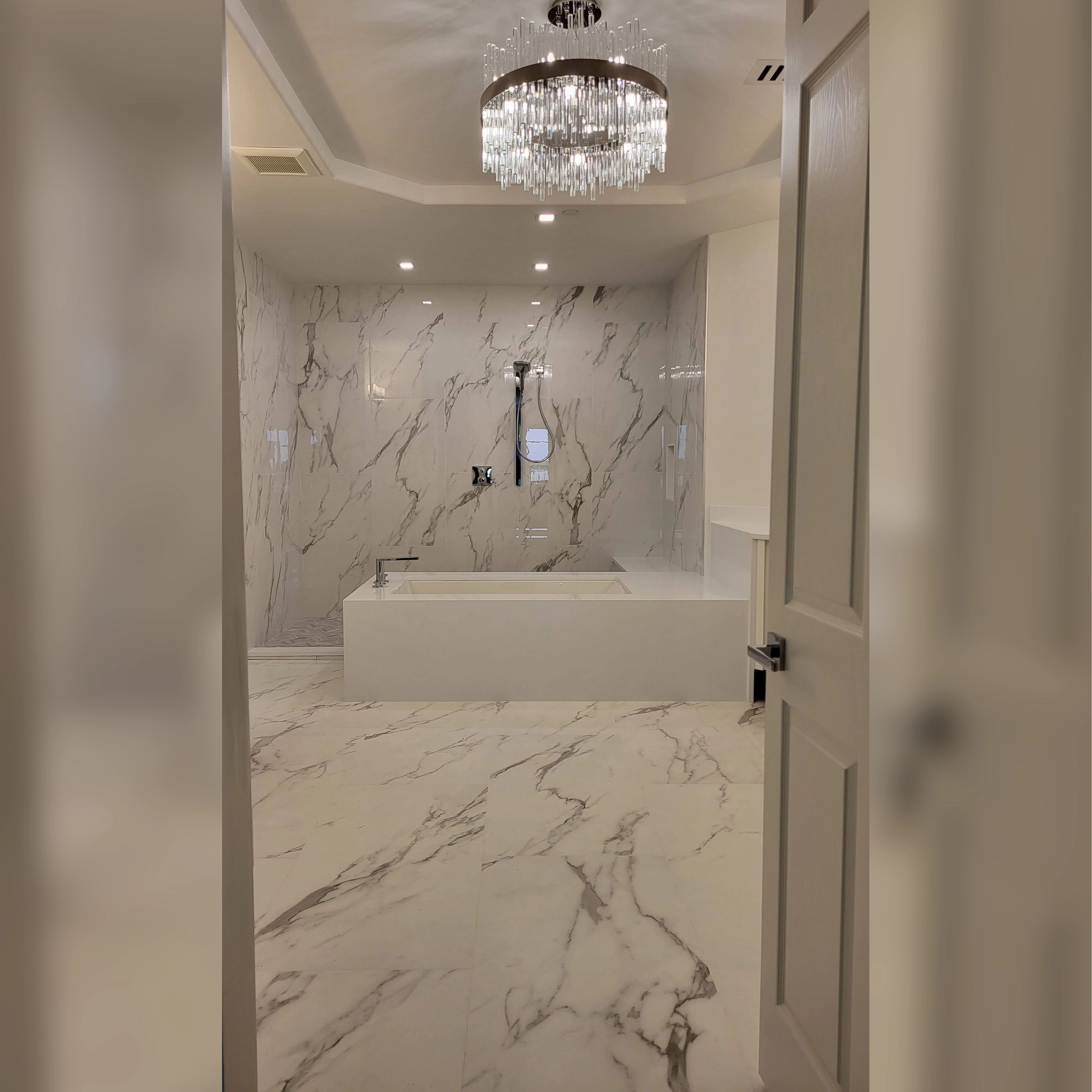 This elegant bathroom features large-format porcelain tiles with a marble-like pattern, extending seamlessly from the shower walls to the floor, creating a cohesive and luxurious design enhanced by a stunning chandelier.