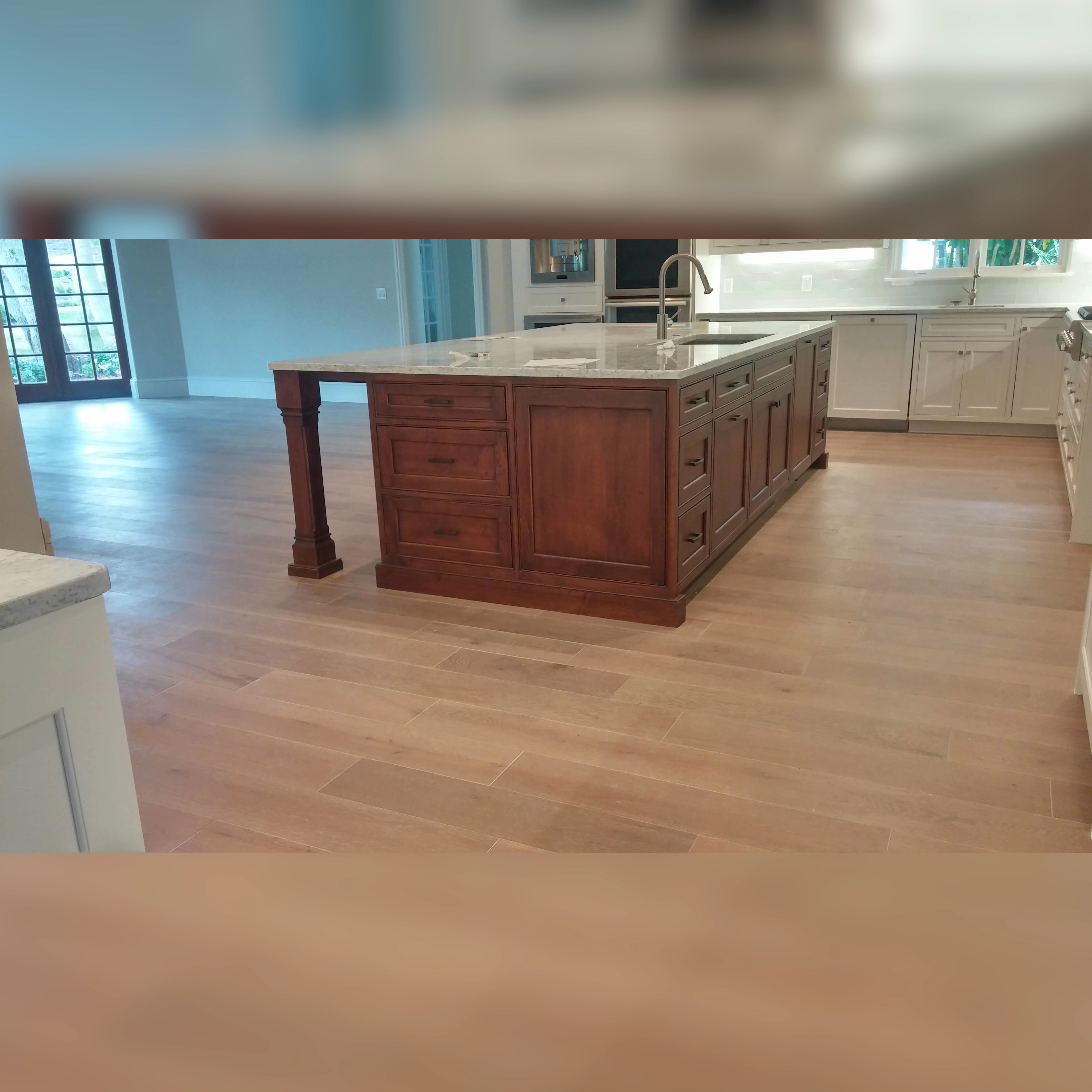 This kitchen features durable engineered wood flooring with a smooth, natural finish, complementing the warm wood tones of the central island and the bright, open design of the space.